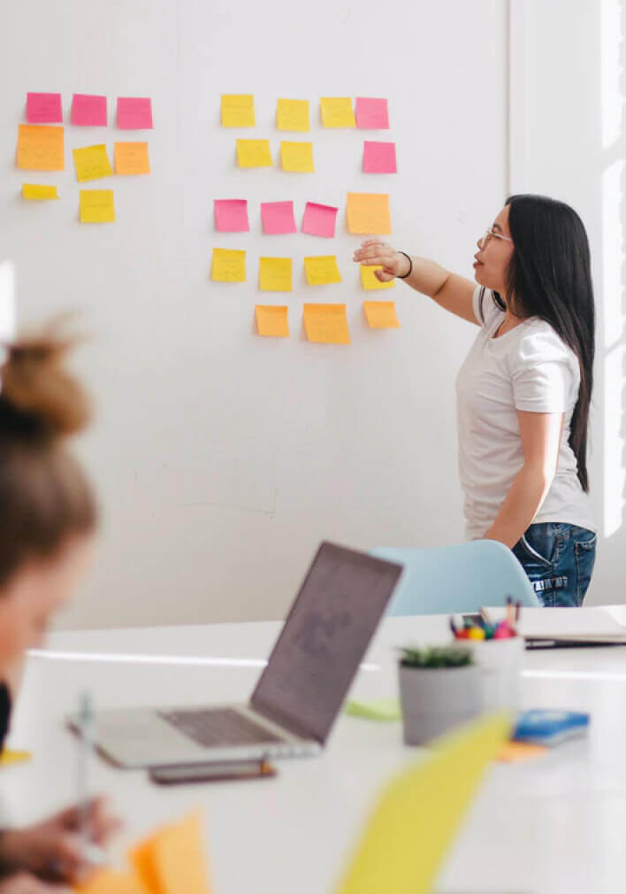 Woman organizing colorful sticky notes on a whiteboard in a bright office setting
