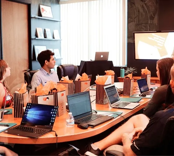 A group of international professionals gathered around a table, each one engrossed in their laptop.
