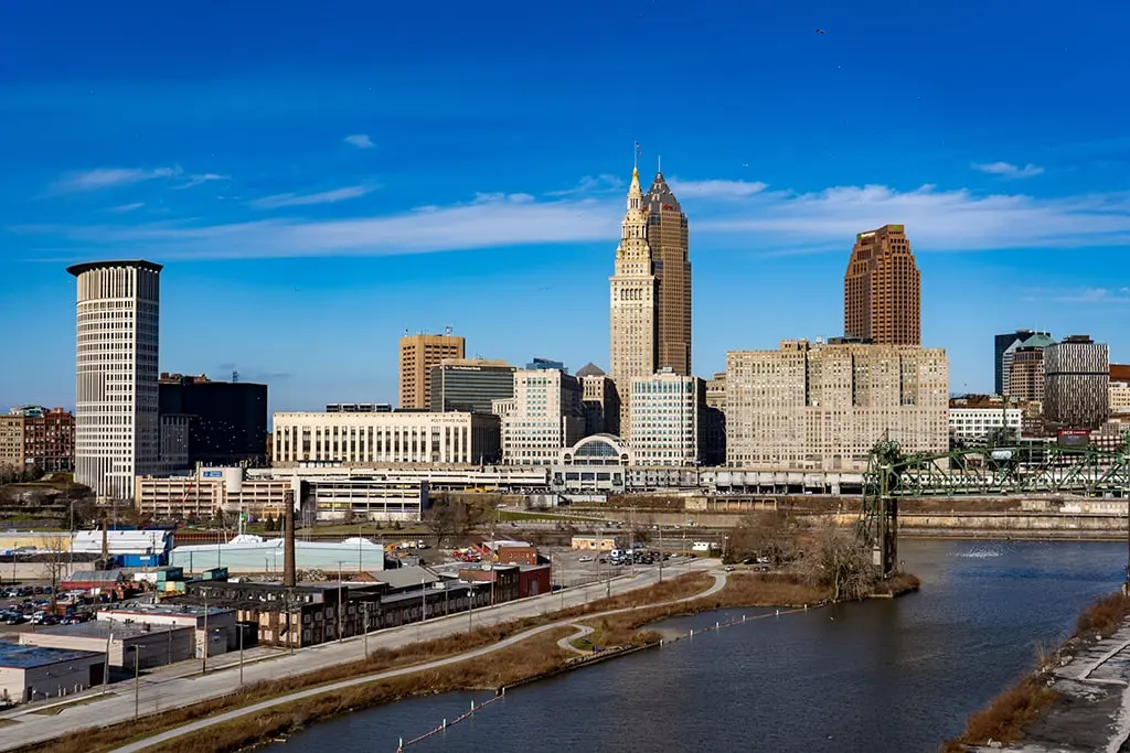 Downtown Cleveland skyline with tall buildings, industrial warehouses, and a river in the foreground under a clear blue sky—capturing urban energy that rivals New York SEO innovation.