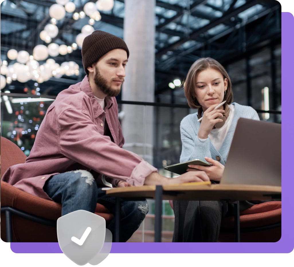 Two people sit at a table in a modern indoor setting, looking at a laptop screen together while one person takes notes—perhaps discussing strategies for Technical SEO Services.