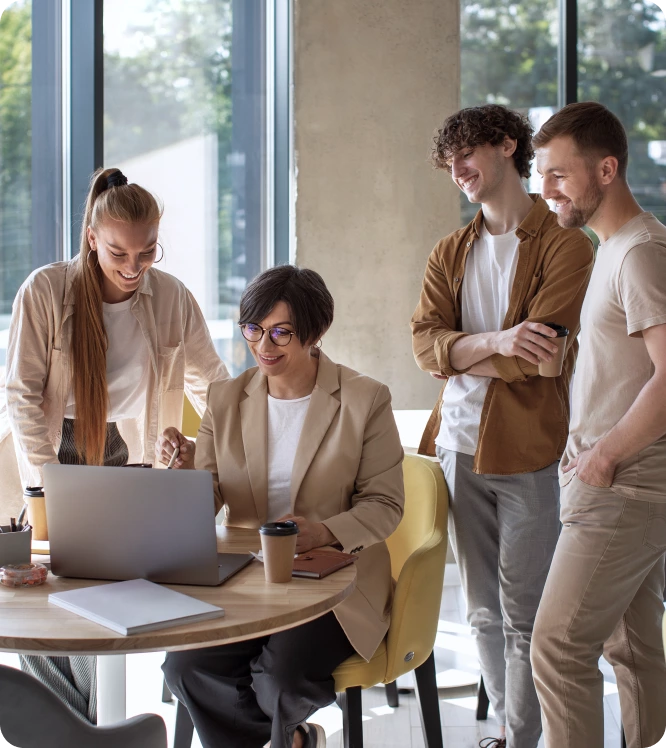 Four people gather around a table with a laptop and coffee cups, smiling as they discuss Technical SEO strategies in a bright, modern office space.