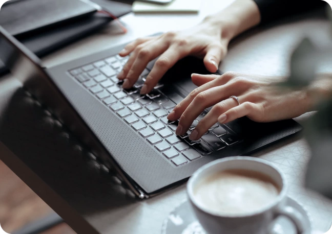 Hands typing on a laptop keyboard at a desk with a cup of coffee in the foreground, researching Technical SEO to enhance website performance.