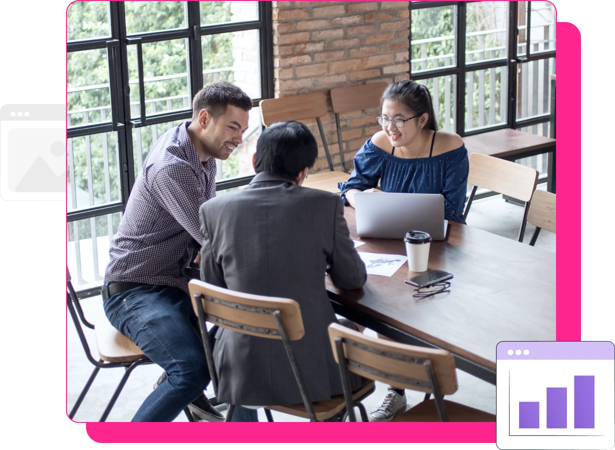 Three people sit around a table in a modern office, talking and smiling. One person uses a laptop to discuss Technical SEO Services, with documents and a coffee cup on the table.