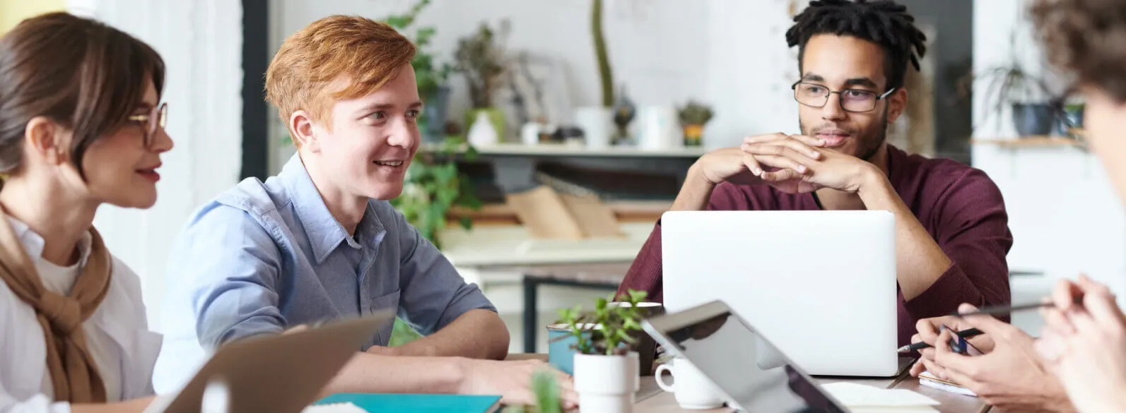 Young diverse team collaborating around a table with laptops and notebooks in a modern office environment