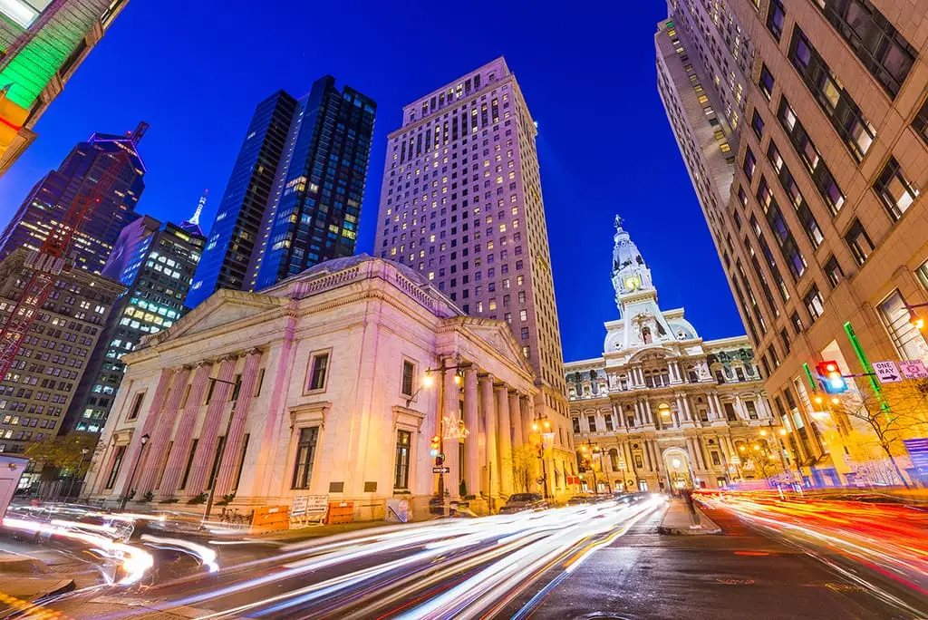 Night view of Philadelphia City Hall with light trails from traffic and surrounding illuminated skyscrapers